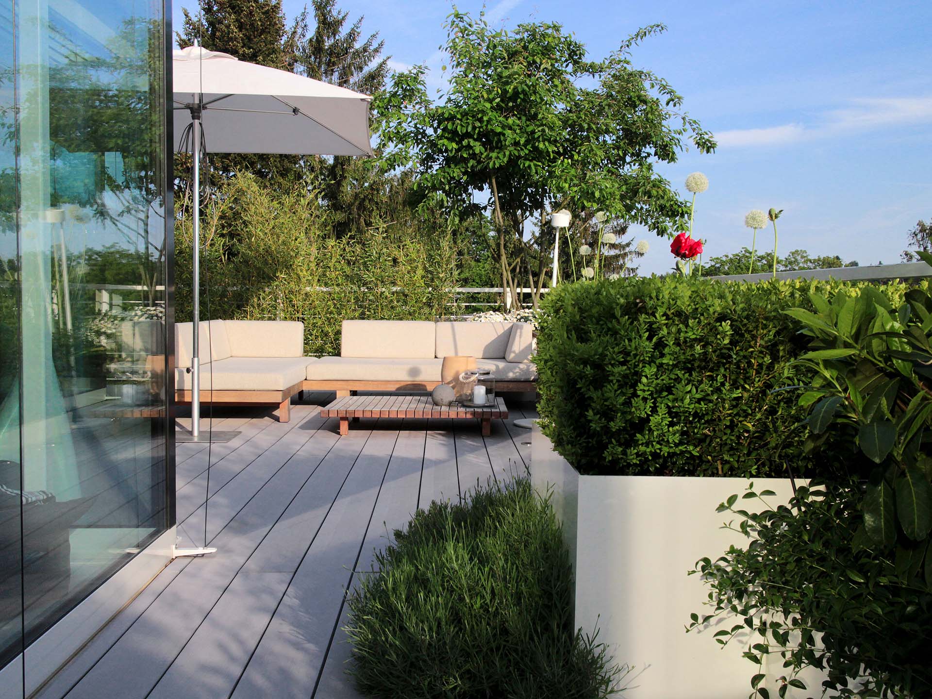 Terrasse mit grauen WPC Terrassenbelag und modernen Möbeln und viel Begrünung